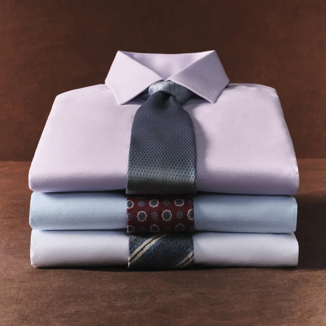 Stacked folded dress shirts in lilac and pale blue tied with a dark tie