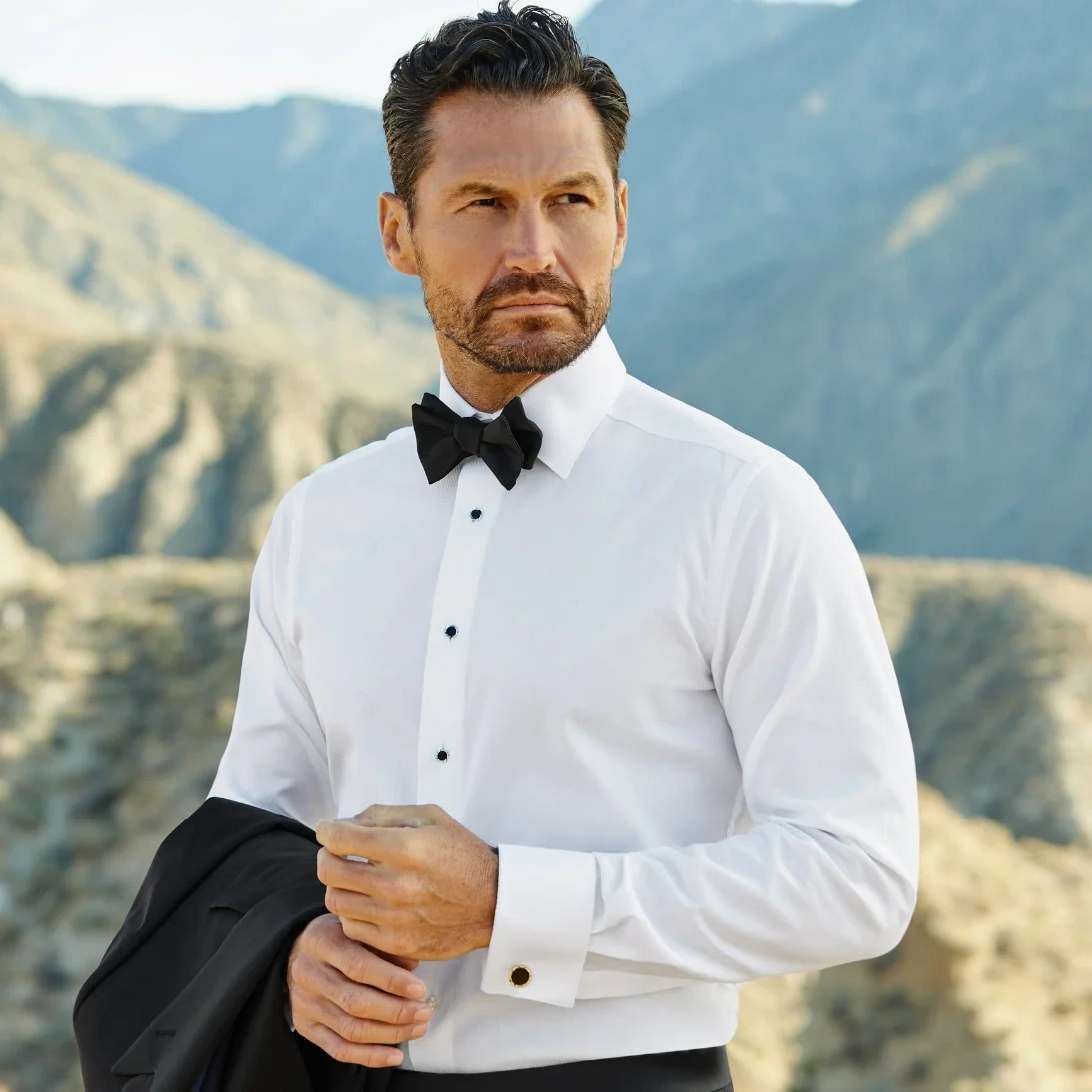 A man in a white formal shirt and black bow tie against mountains