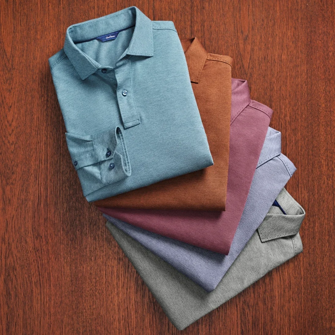 Fanned long sleeve polos in teal, rust, plum and grey on a wooden table