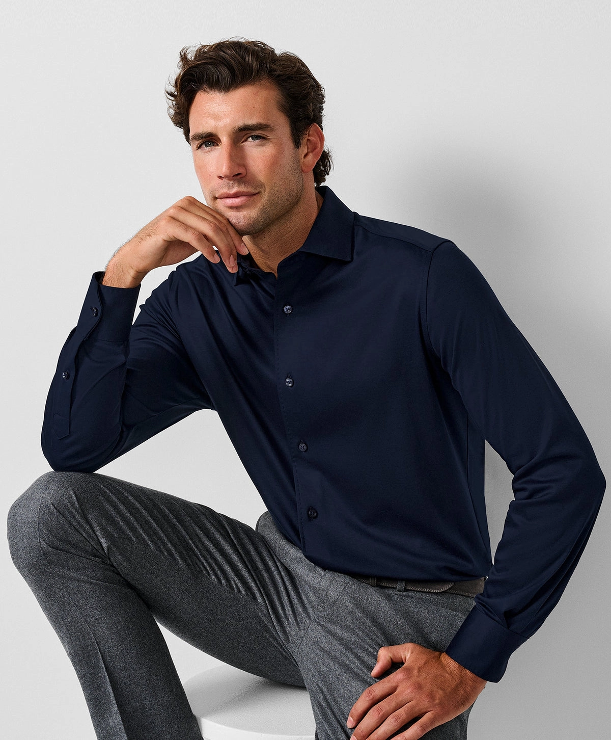 A man in a dark navy long sleeve polo seated against a grey backdrop