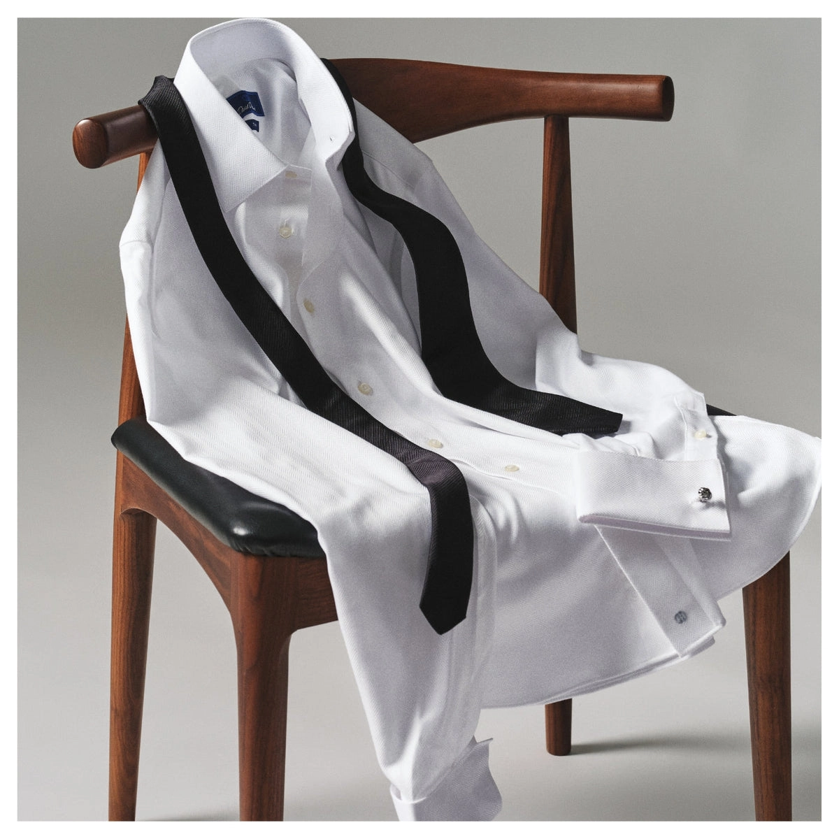A white tuxedo shirt with black stripes draped over a wooden chair
